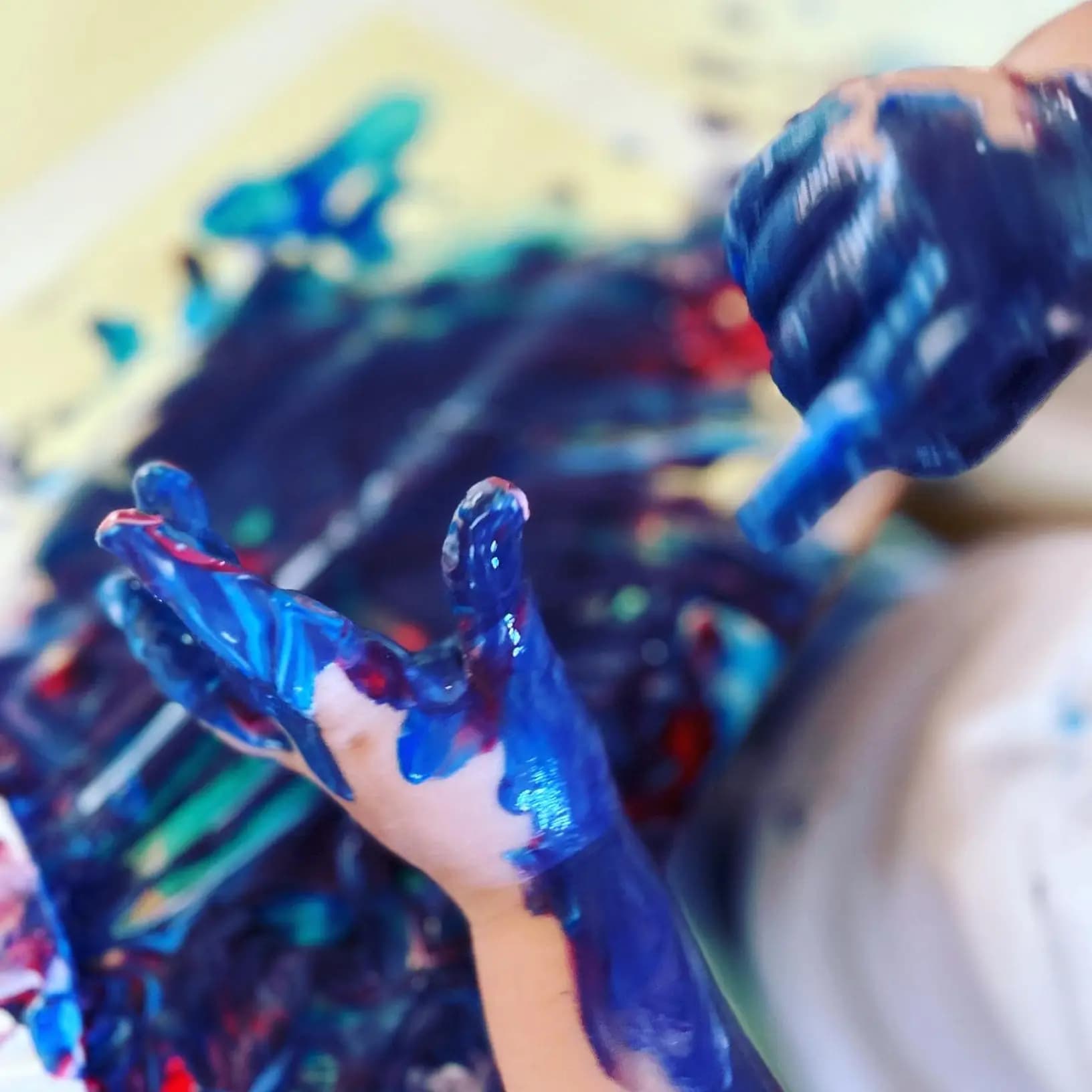 Child’s paint-covered hands held above a messy painting during a learning-through-play activity at Moolanda